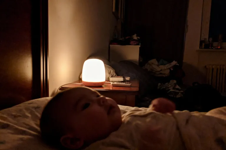 Bébé couché dans une chambre sombre, éclairée faiblement par une lampe de chevet allumée, ambiance paisible.
