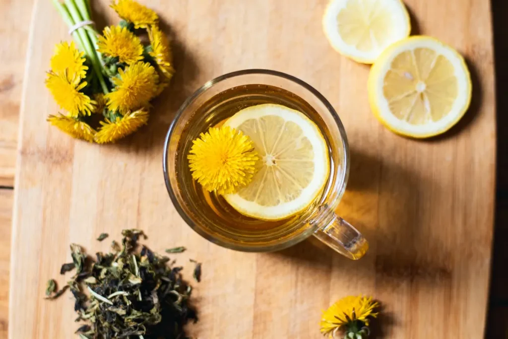 Tasse de tisane au pissenlit et citron sur planche, fleurs et feuilles séchées à côté.