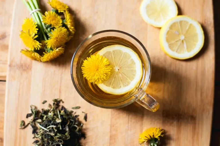 Tasse de tisane au pissenlit et citron sur planche, fleurs et feuilles séchées à côté.