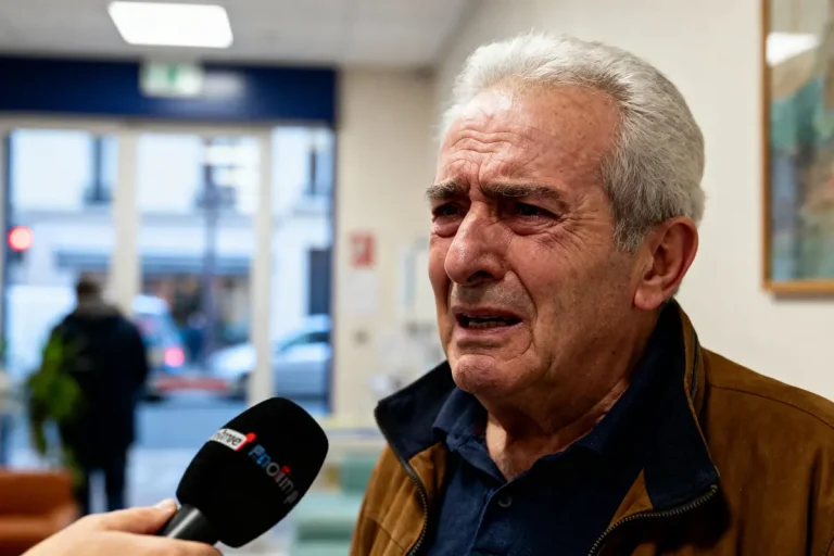 Homme âgé ému parlant à un micro dans un intérieur flou, visage exprimant forte émotion.