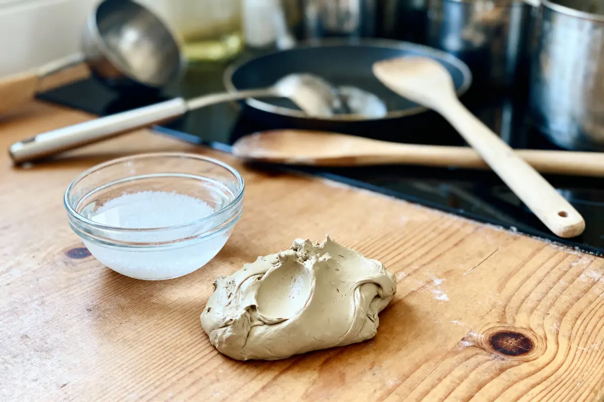 Pâte marron, bol de sel, cuillère en bois sur plan de travail de cuisine.