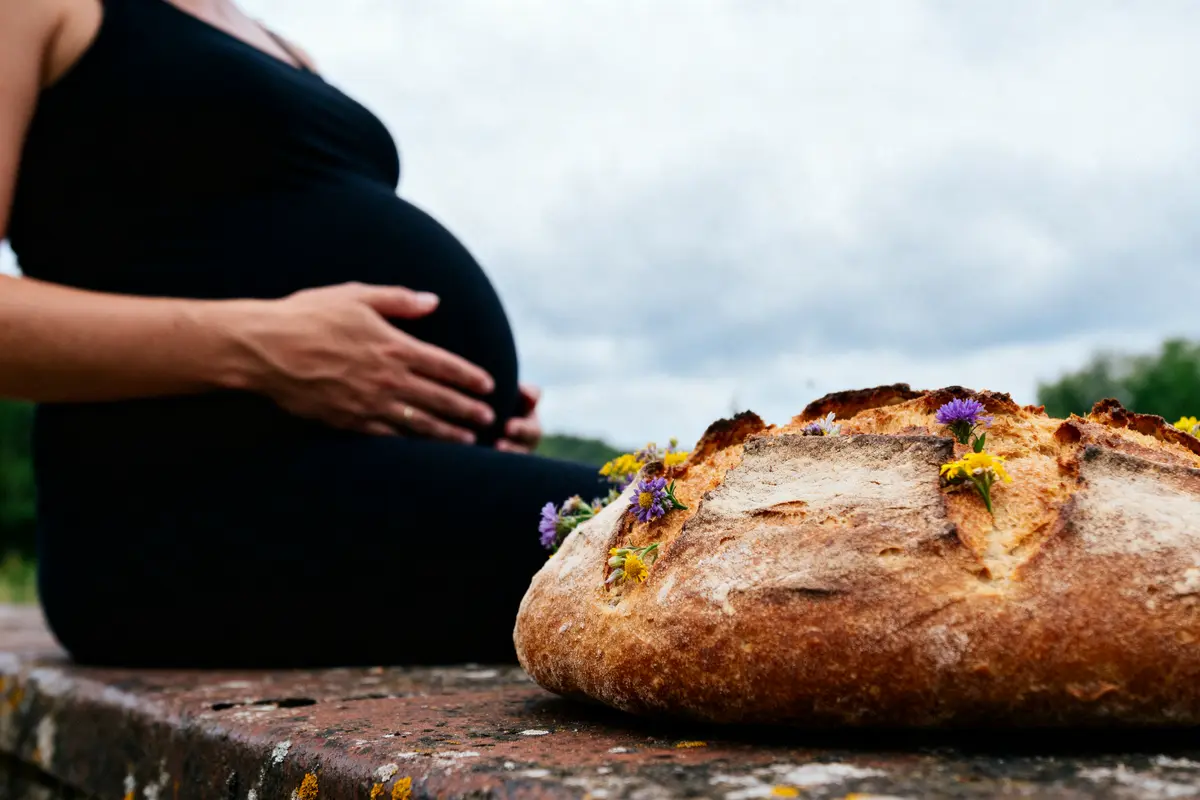 Une femme enceinte assise à côté d'un pain décoré de fleurs sur une table extérieure.