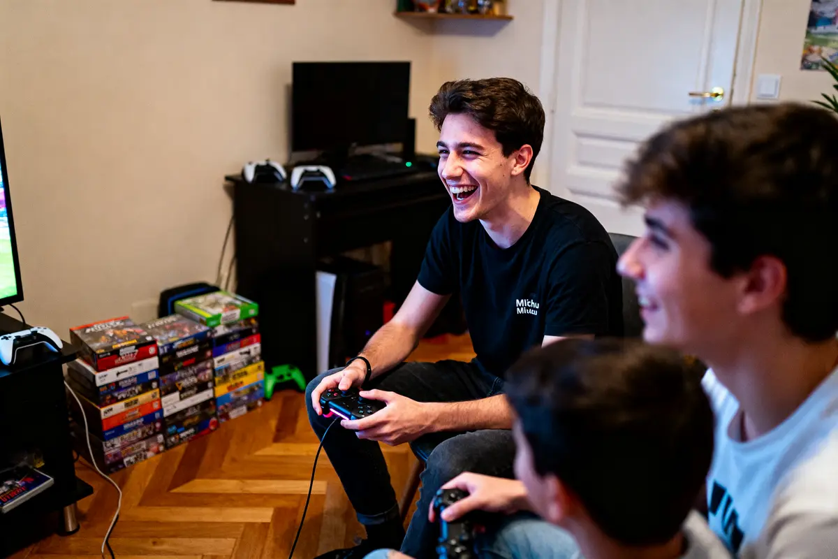 Trois jeunes souriants jouent à des jeux vidéo dans un salon, manettes à la main.