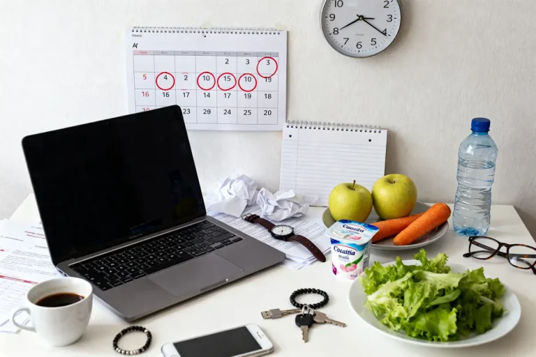Bureau avec ordinateur, aliments sains et agenda suggérant des causes de la proctalgie fugace possibles