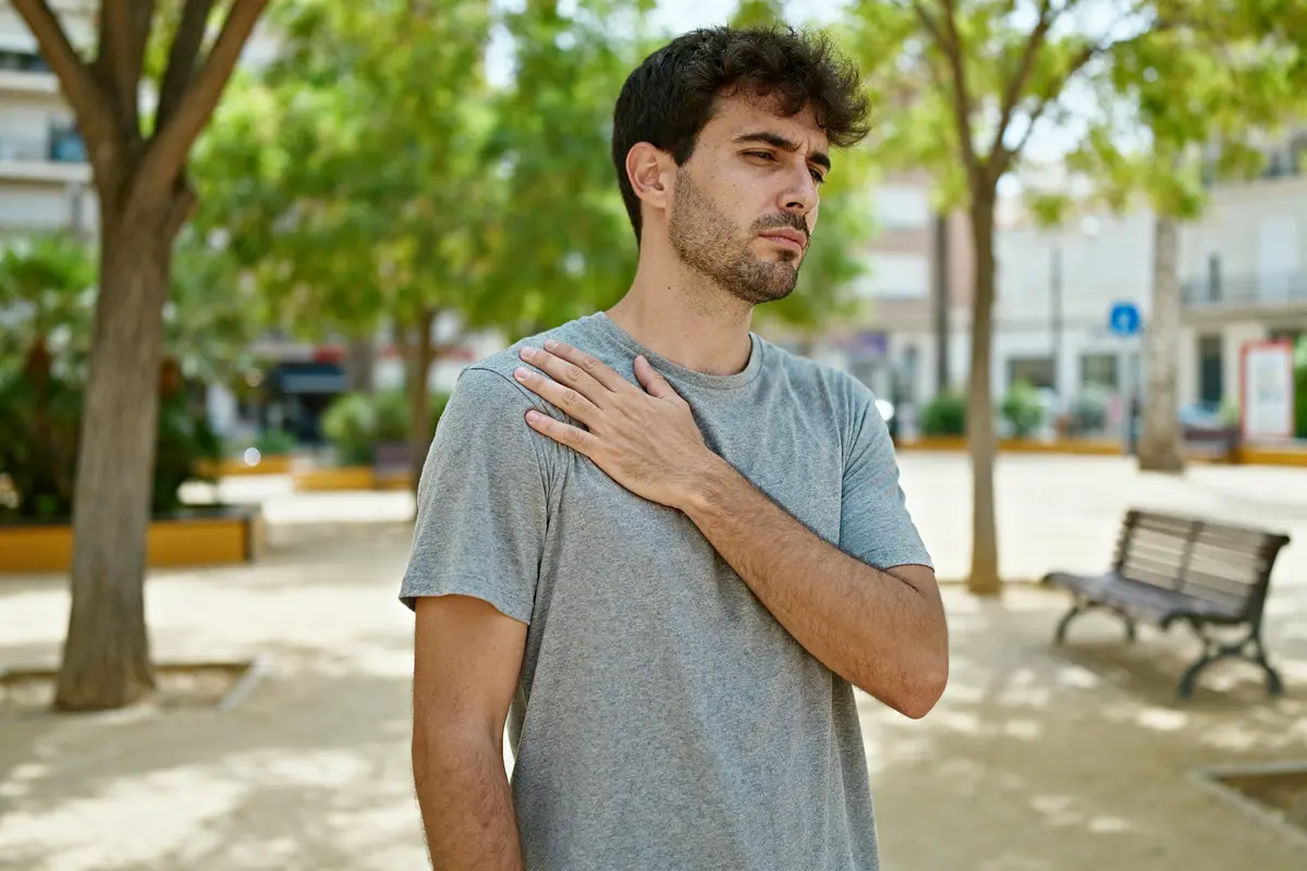 Un homme ressent une douleur à l'omoplate droite dans un parc extérieur.