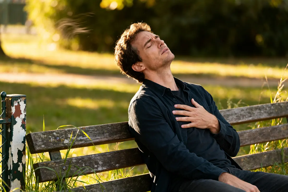 Homme sur un banc extérieur, main sur le cœur, rêver d'une crise cardiaque.