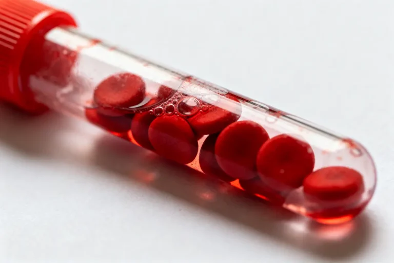 Tube à essai avec des globules rouges flottant dans un liquide transparent, fond blanc.