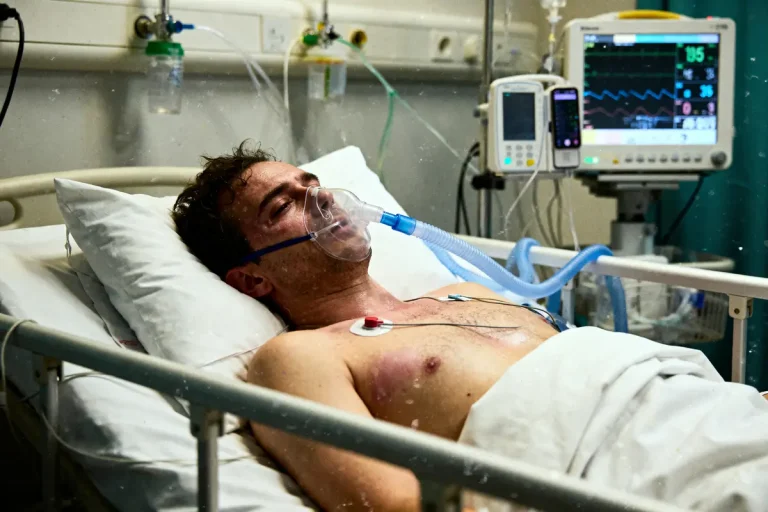 Homme allongé dans un lit d'hôpital, portant un masque à oxygène, connecté à un moniteur médical.