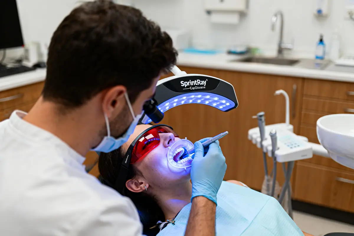 Dentiste effectuant un traitement dentaire avec une lumière bleue pour durcir le matériau, patient portant lunettes.