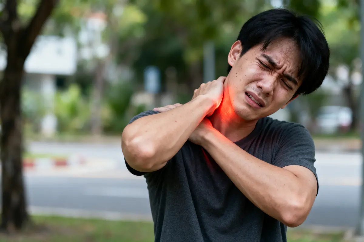 Homme souffrant de douleur cervicale, tenant son cou, fond flou en extérieur.