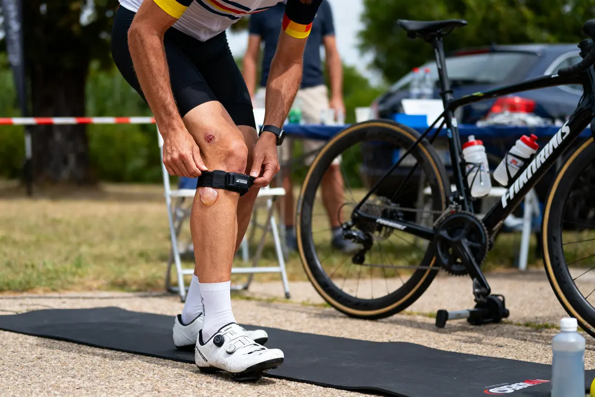 Cycliste ajustant bracelet au genou, près d'un vélo, lors d'une compétition en plein air.