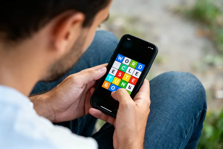 Un homme joue à un jeu de lettres colorées sur un smartphone.
